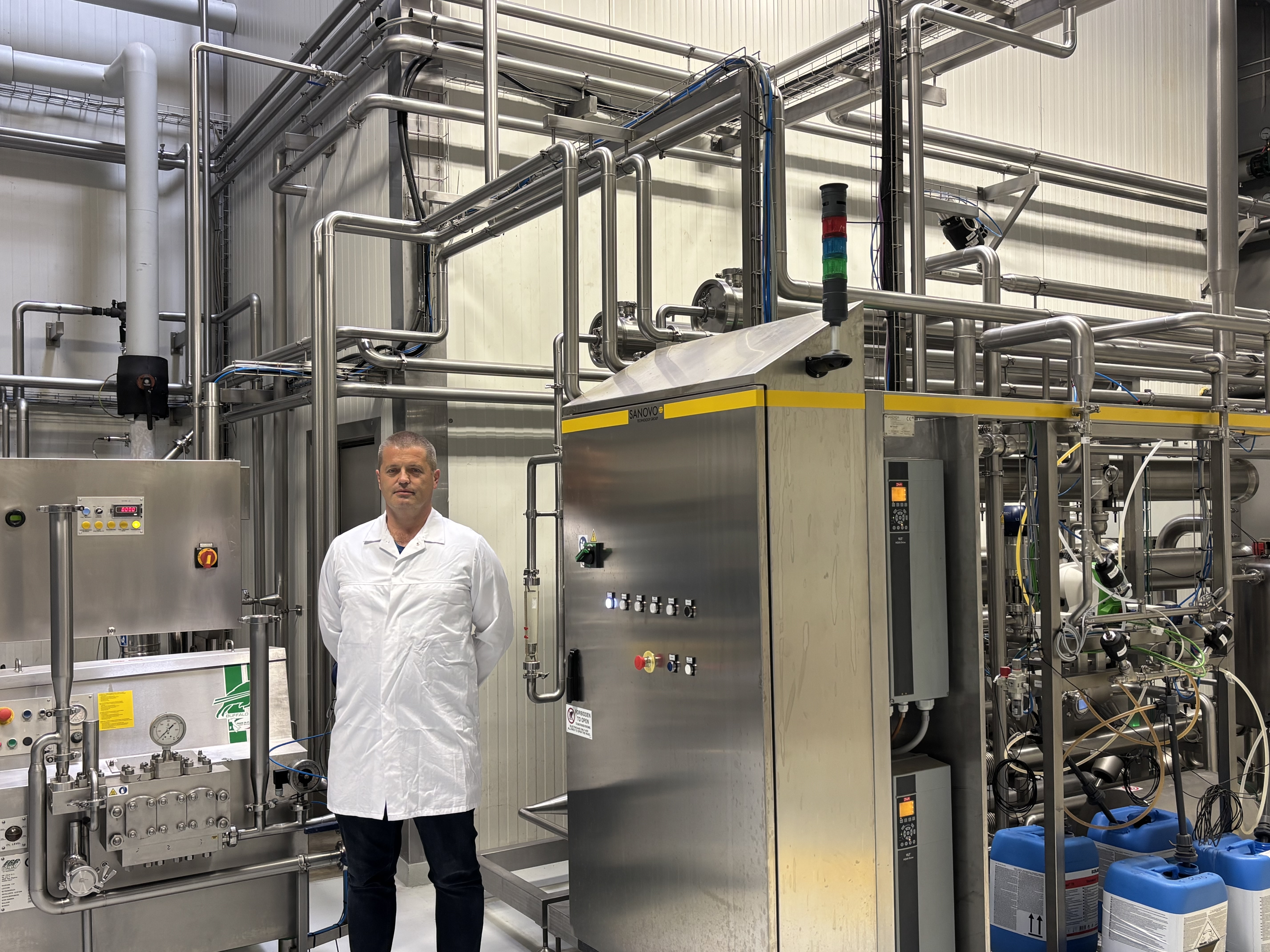 Operator standing next to SANOVO industrial pasteurizer and heat treatment system in a processing plant.