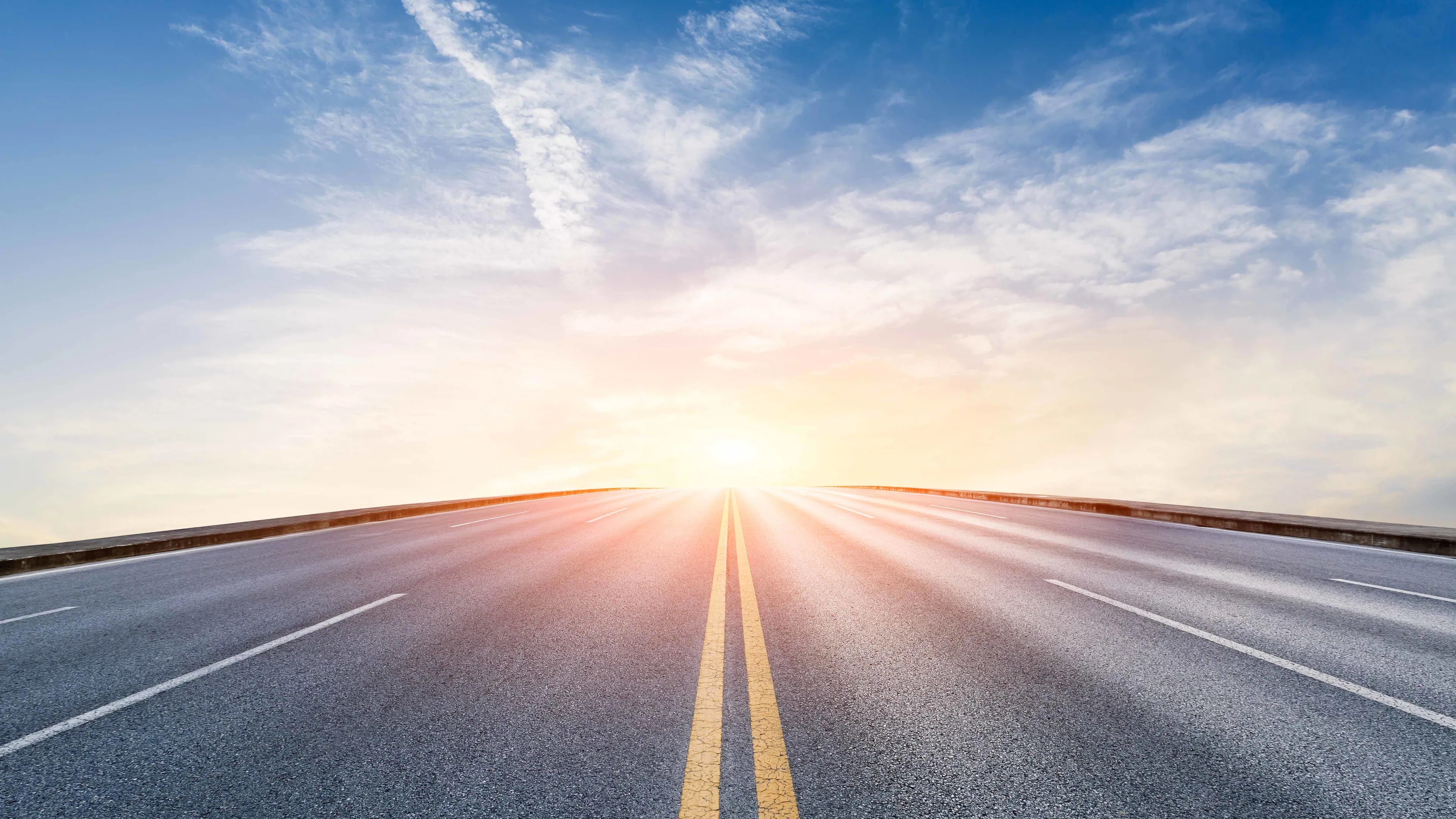 Empty road leading toward the horizon with sunrise and blue sky