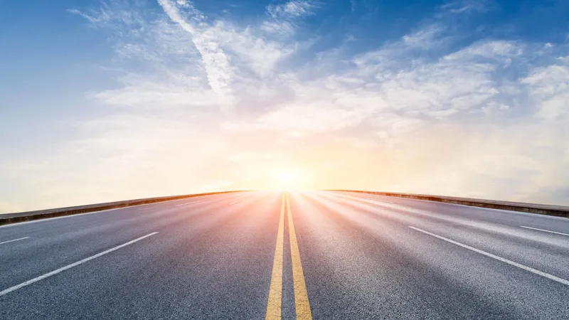 Empty road leading toward the horizon with sunrise and blue sky