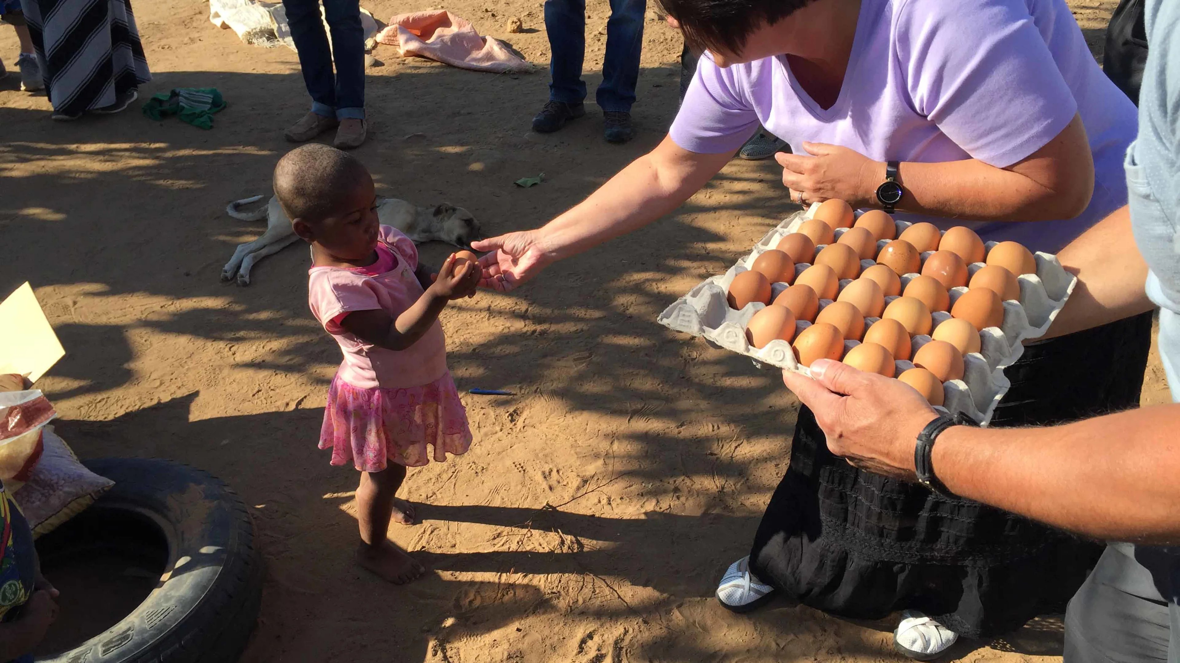 Woman handing eggs to little girl.