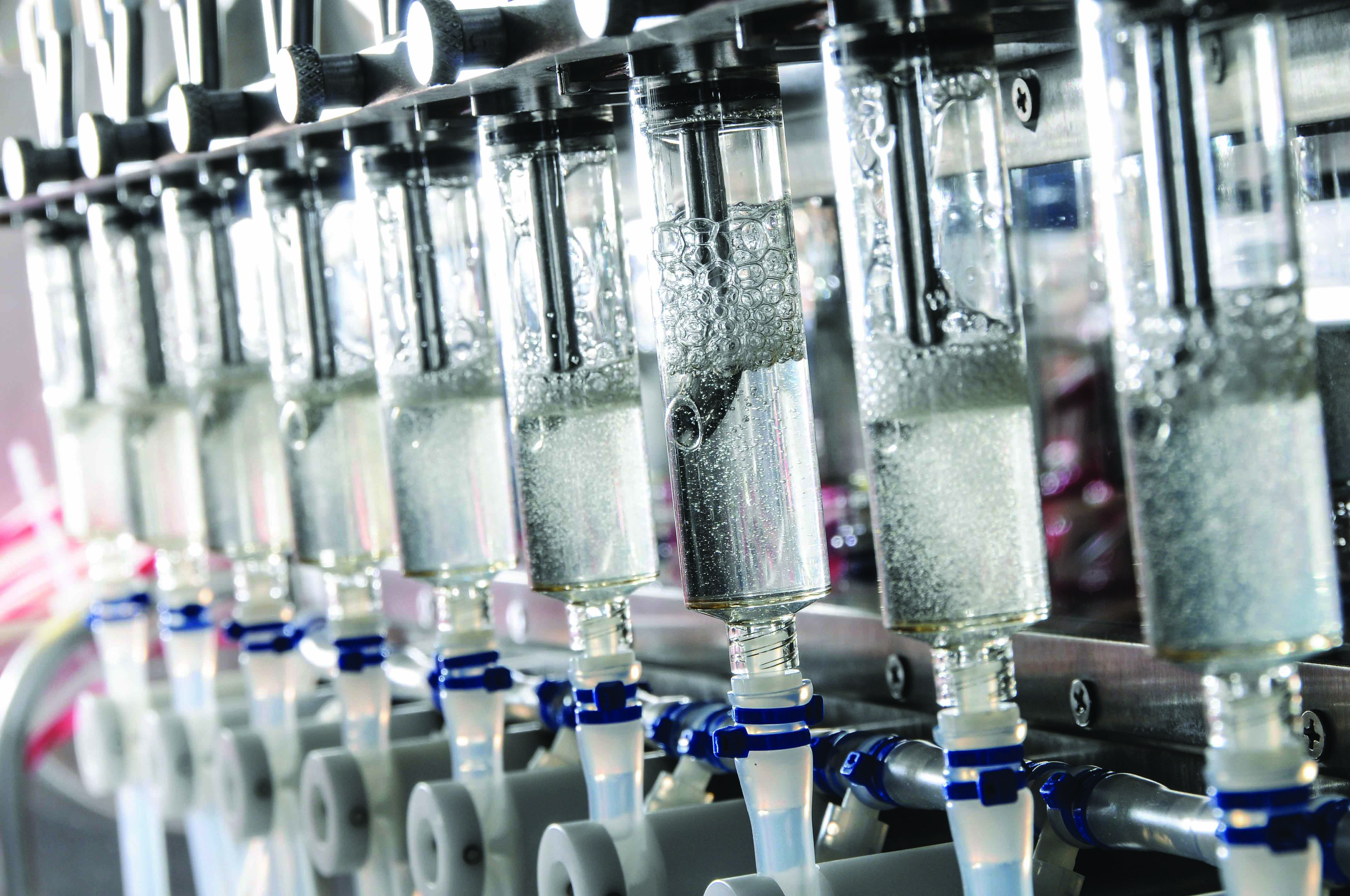 Close-up of transparent liquid-filled cylinders and tubing inside vaccine production equipment.
