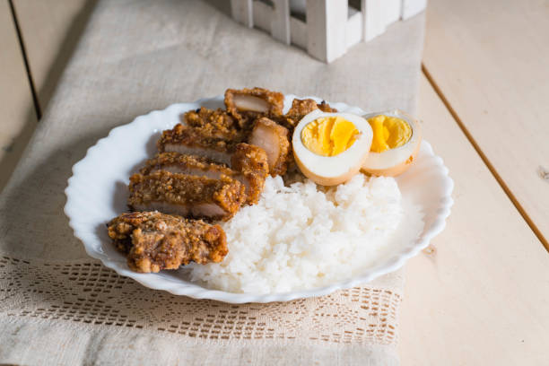 Dish with sliced meat, rice, and boiled eggs on a wooden table.