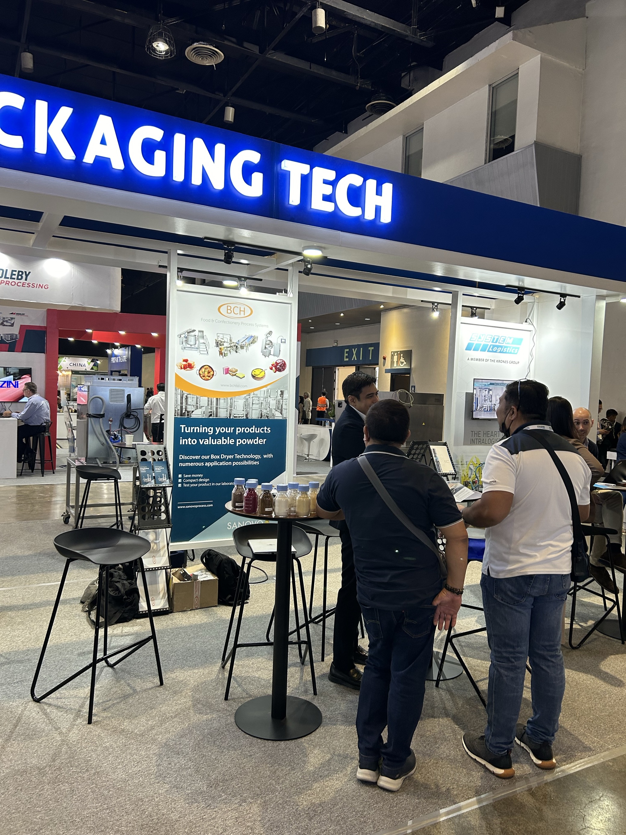 People at the SANOVO TECHNOLOGY PROCESS stand at an expo discussing food and ingredient processing technologies.