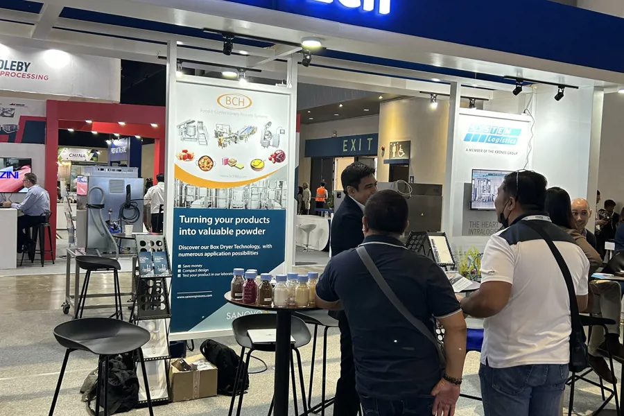 People at the SANOVO TECHNOLOGY PROCESS stand at an expo discussing food and ingredient processing technologies.
