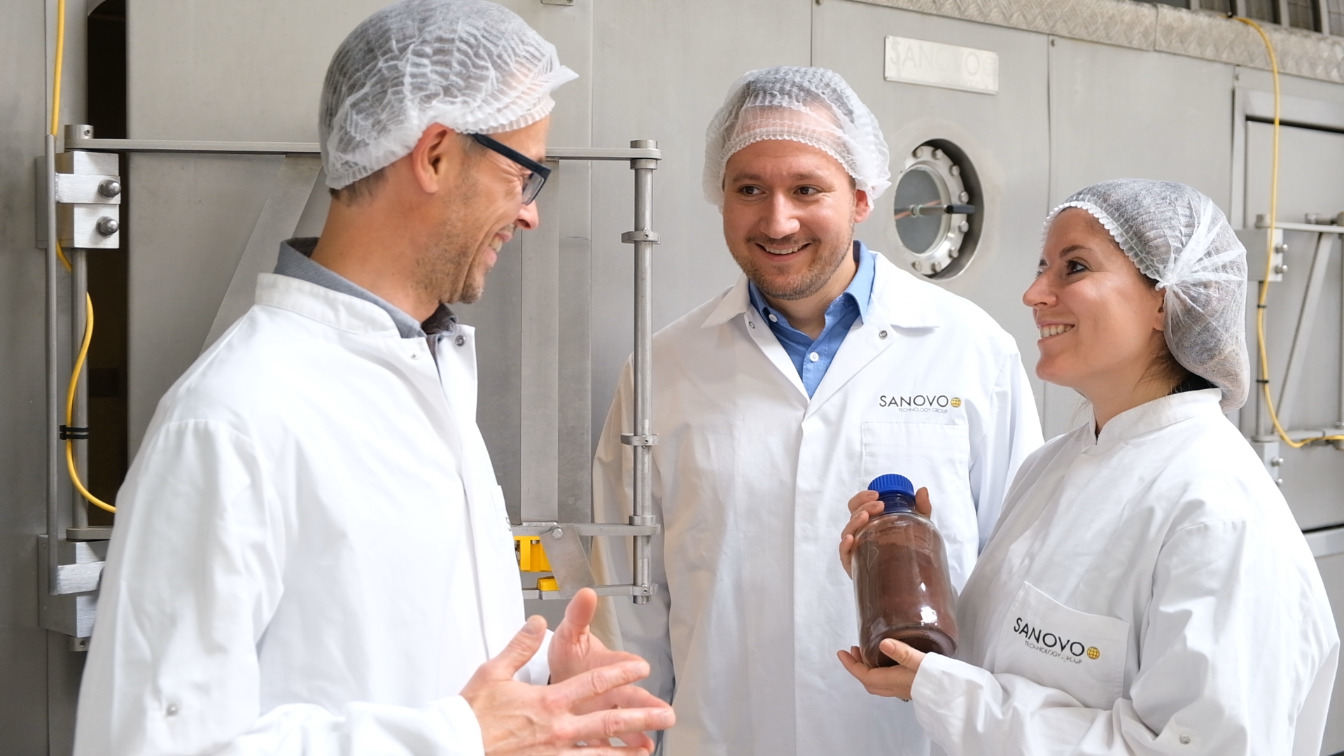 Operators collaborating near spray drying machinery with a finished powder product.