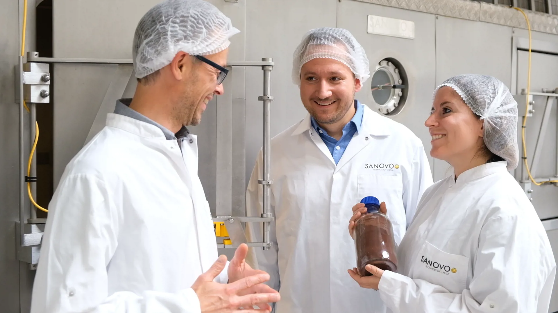 Operators collaborating near spray drying machinery with a finished powder product.