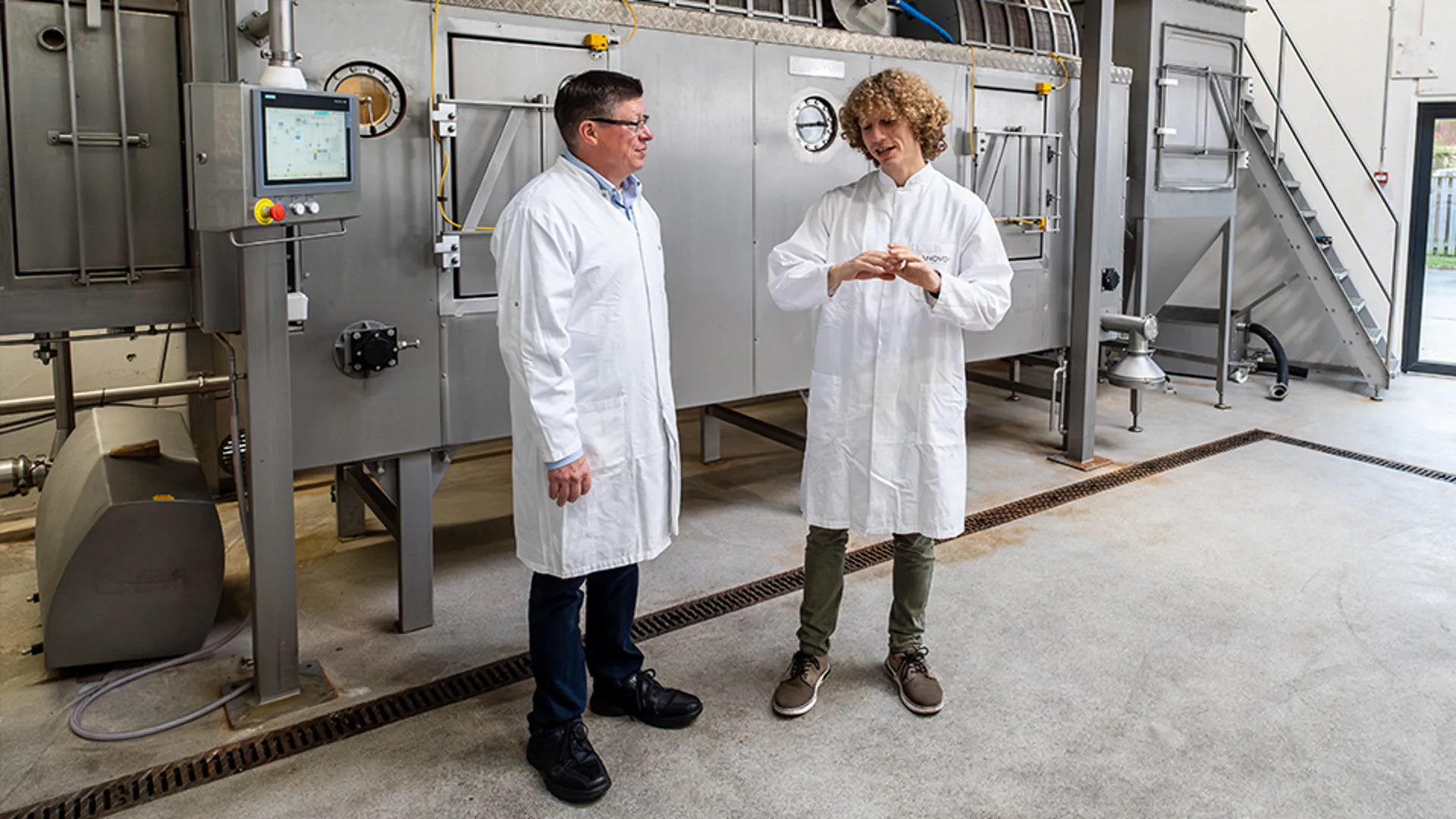 SANOVO technicians in lab coats discussing spray drying equipment inside.