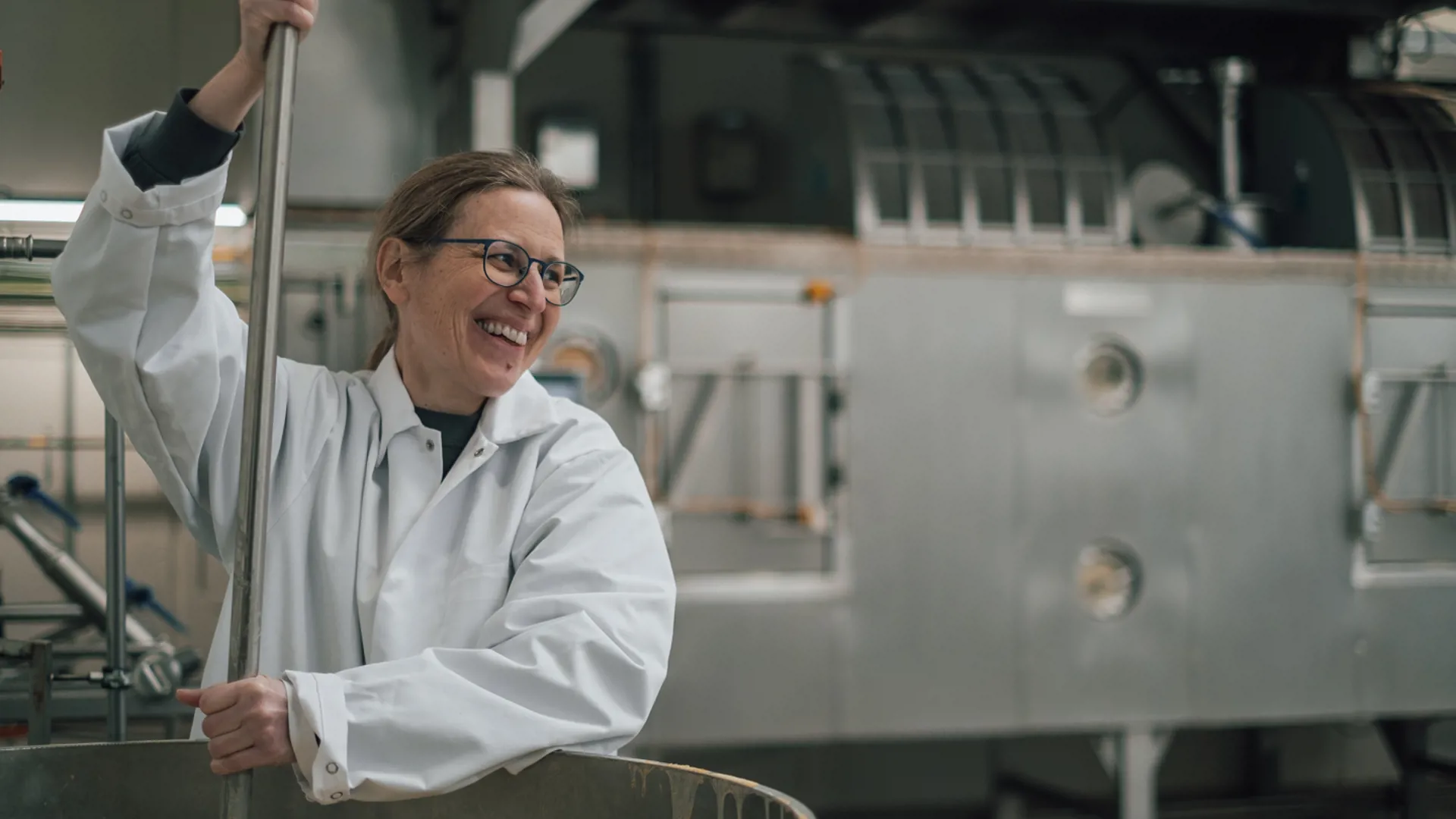 Technician mixing product in a processing tank near industrial drying equipment.
