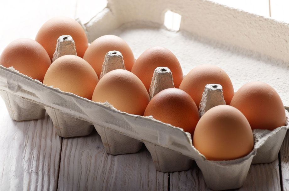 Cardboard egg carton filled with brown shell eggs on a wooden table.