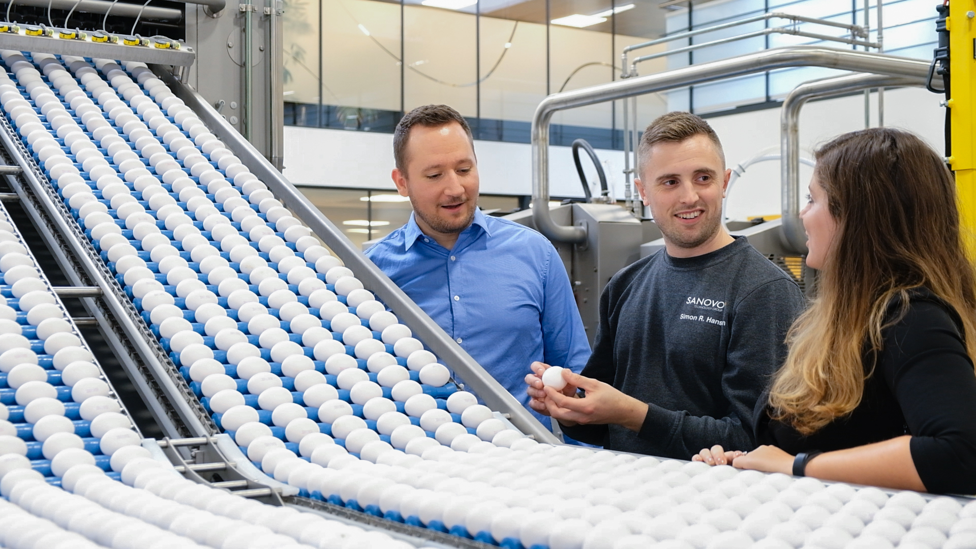Three people discussing eggs by a SANOVO machine
