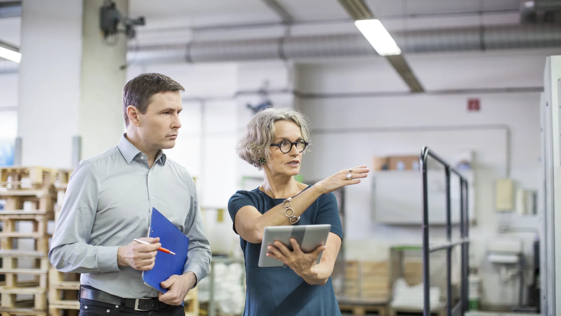 Two people reviewing operations in a factory with tablet and documents.