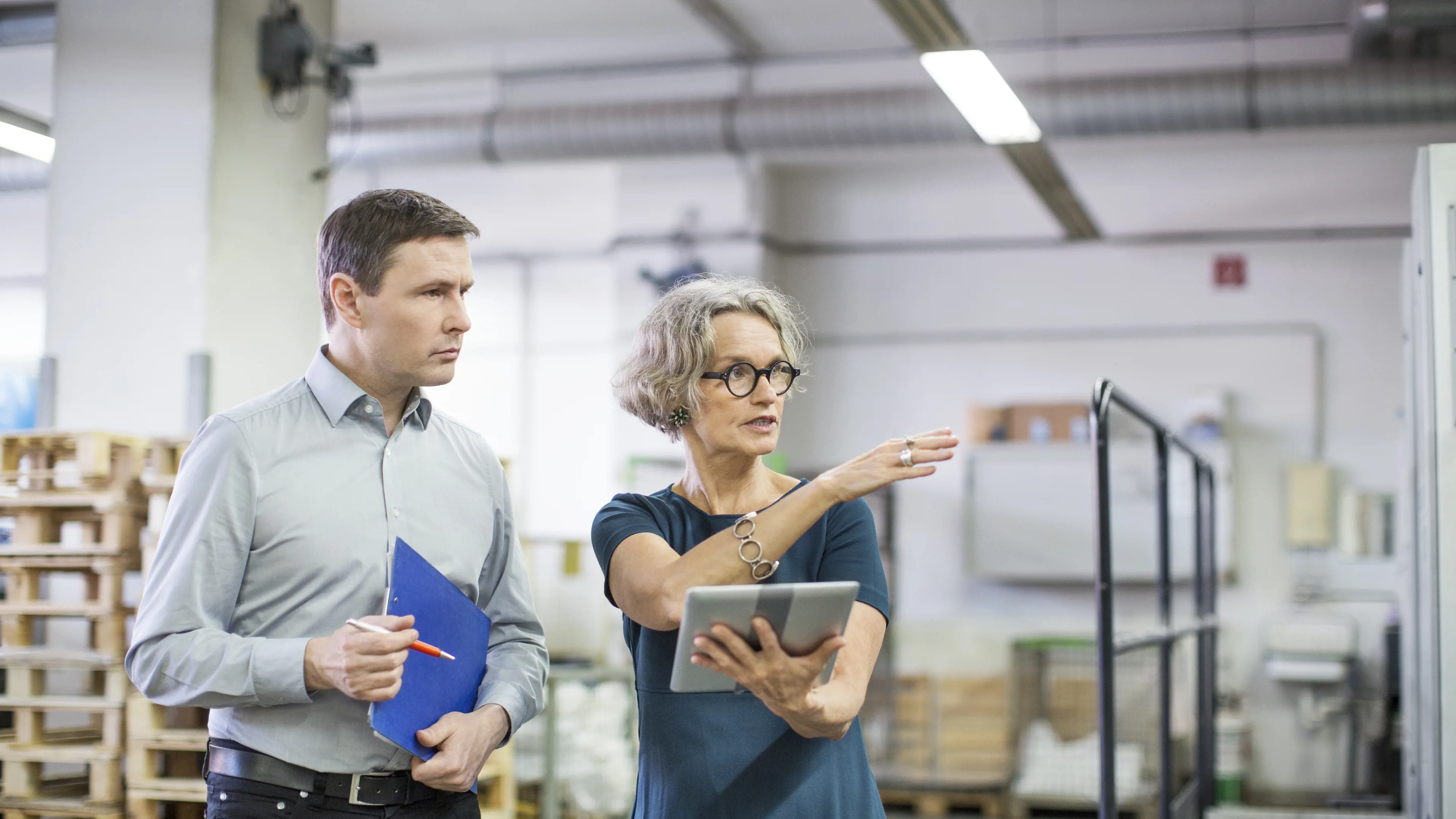 Two people reviewing operations in a factory with tablet and documents.