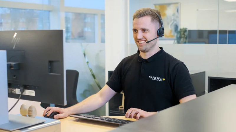 SANOVO support specialist assisting a customer remotely at an office workstation.