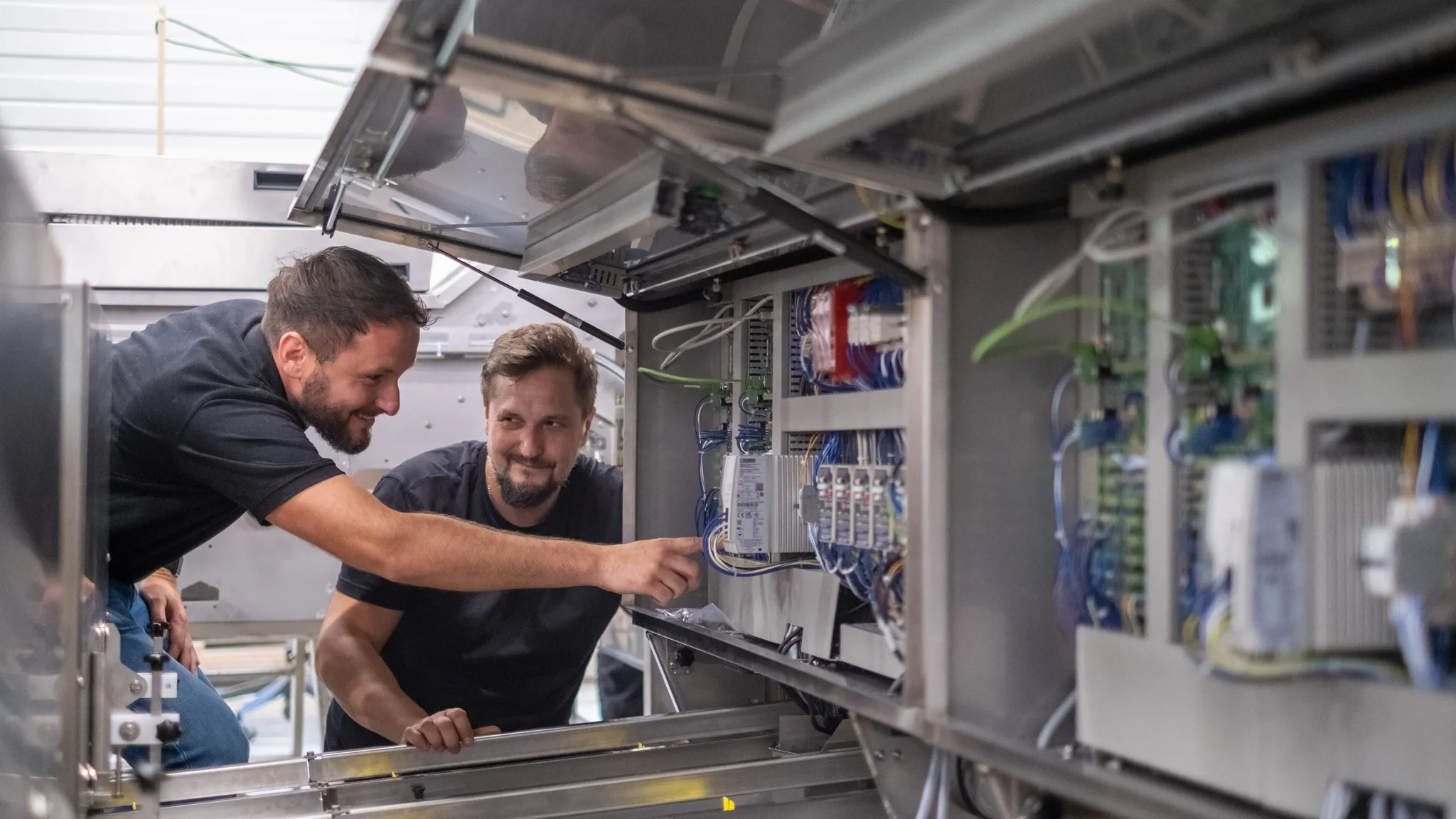 Two technicians inspecting electrical components inside a machine